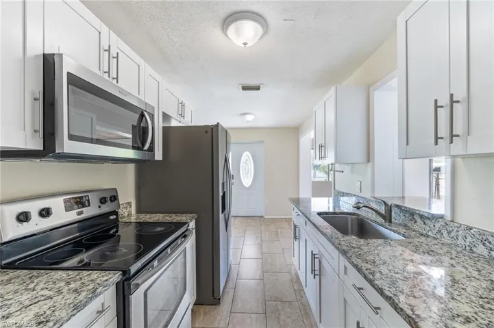 Kitchen featuring appliances with stainless steel finishes, plenty of natural light, white cabinetry, a textured ceiling, and light stone counters