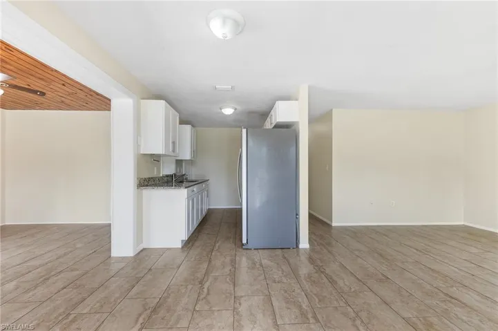 Kitchen with freestanding refrigerator, white cabinetry, light wood-style flooring, open floor plan, and stone counters