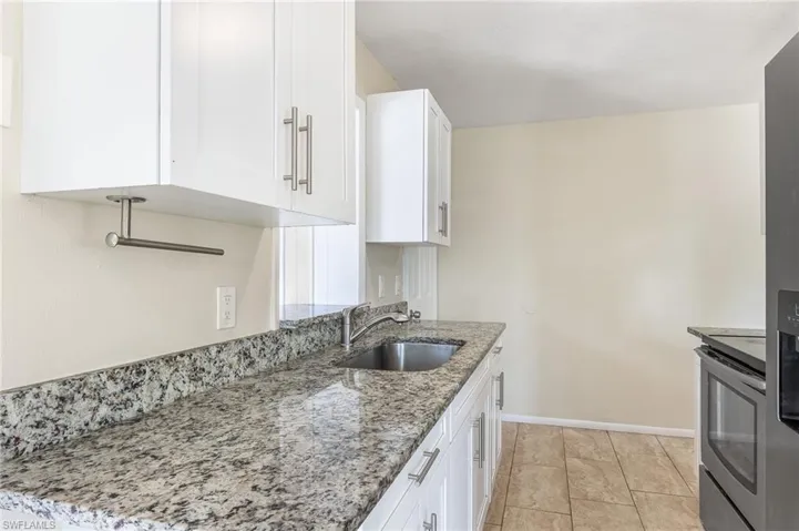 Kitchen featuring stainless steel electric range, white cabinetry, and light stone counters
