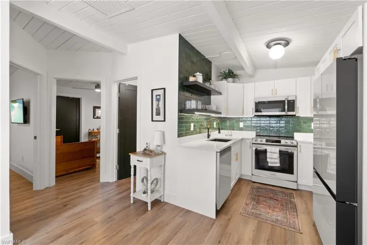 Kitchen featuring sink, white cabinetry, tasteful backsplash, stainless steel appliances, and beam ceiling
