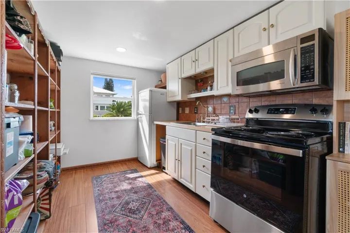 Kitchen with sink, white cabinetry, stainless steel appliances, decorative backsplash, and light wood-type flooring