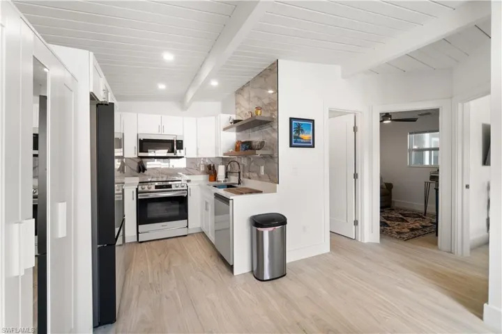 Kitchen with sink, white cabinetry, stainless steel appliances, beam ceiling, and backsplash