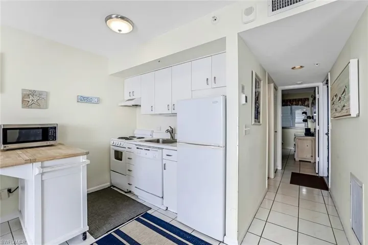Kitchen featuring white appliances, white cabinetry, light tile patterned floors, and butcher block countertops