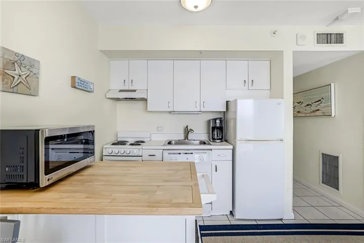 Kitchen with white appliances, white cabinetry, extractor fan, and wooden counters