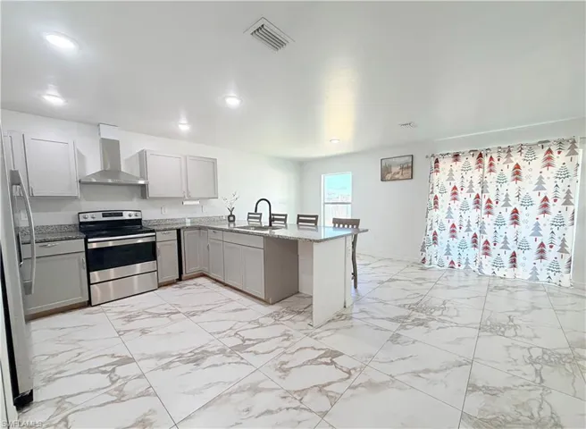 Kitchen with light marble finish floors, gray cabinetry, appliances with stainless steel finishes, a peninsula, and a kitchen breakfast bar
