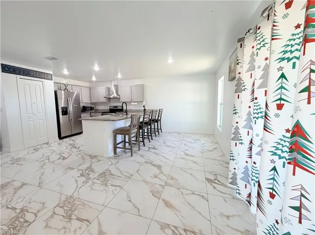 Kitchen featuring light marble finish flooring, stainless steel appliances, a breakfast bar area, light stone countertops, and wall chimney exhaust hood