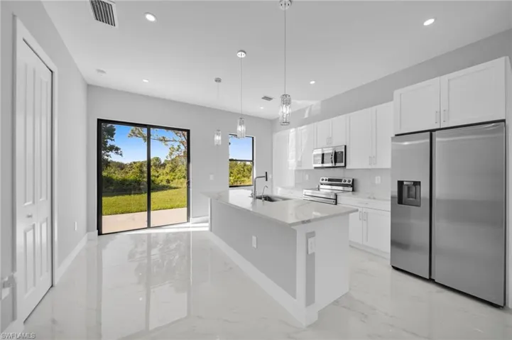 Kitchen featuring stainless steel appliances, white cabinetry, a kitchen island with sink, pendant lighting, and light stone counters