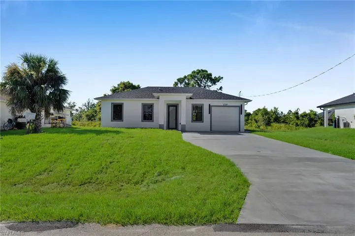 View of front of house with concrete driveway, a front yard, stucco siding, an attached garage, and roof with shingles