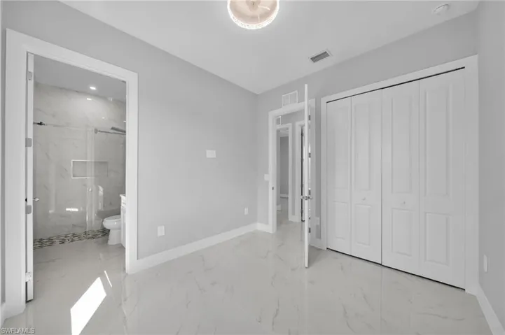 Unfurnished bedroom featuring light marble finish flooring, a closet, and ensuite bath