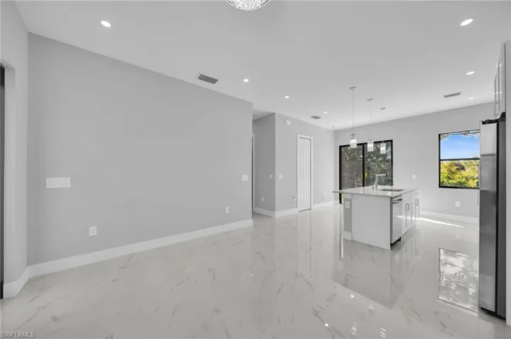 Kitchen with a kitchen island with sink, hanging light fixtures, stainless steel appliances, light stone counters, and white cabinetry