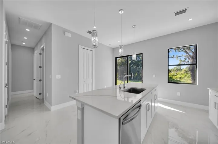 Kitchen featuring hanging light fixtures, stainless steel dishwasher, light stone counters, and light marble finish flooring