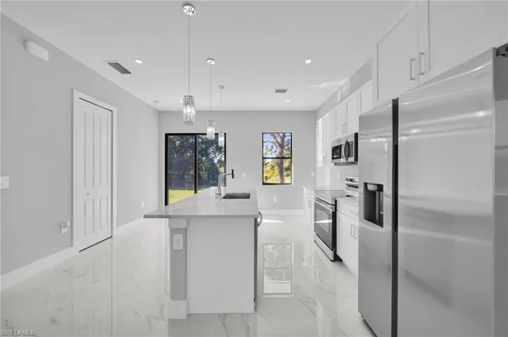 Kitchen with stainless steel appliances, white cabinetry, a center island with sink, hanging light fixtures, and light marble finish floors