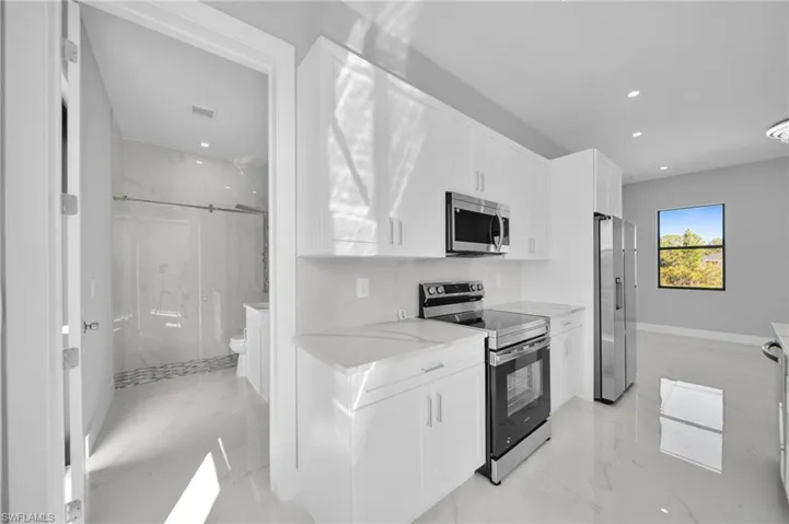Kitchen featuring stainless steel appliances, white cabinetry, recessed lighting, light marble finish flooring, and light stone counters