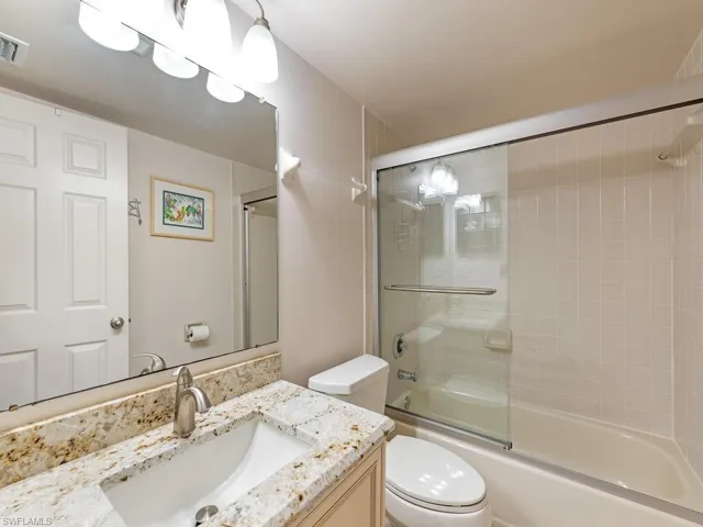 Full bathroom with bath / shower combo with glass door, toilet, and vanity