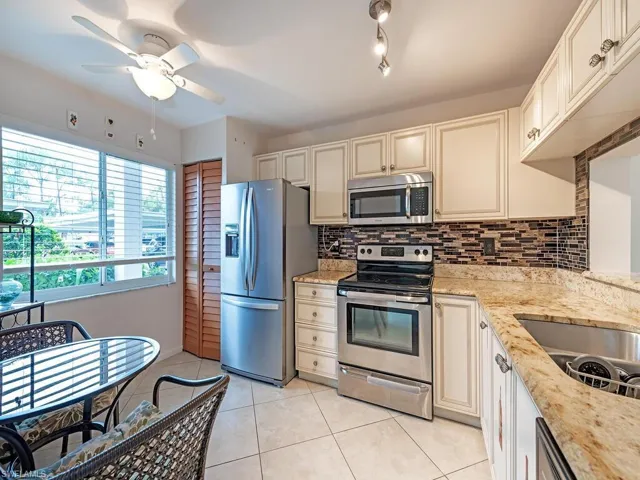 Kitchen featuring appliances with stainless steel finishes, light stone countertops, ceiling fan, and light tile patterned floors
