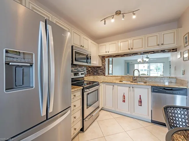 Kitchen featuring light tile patterned flooring, sink, light stone counters, appliances with stainless steel finishes, and track lighting