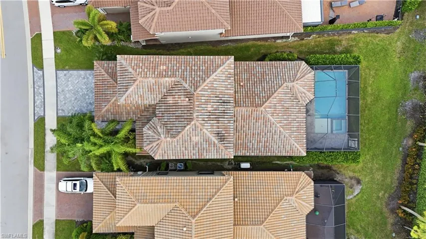Aerial perspective of a residence featuring a clay tile roof, a screened-in swimming pool enclosure, and paved driveway