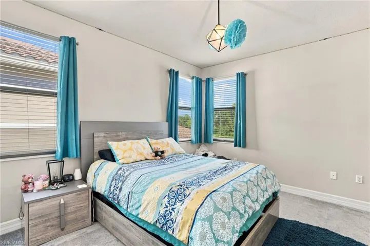 Room featuring neutral walls, wall-to-wall carpeting, geometric pendant lighting, and multiple windows with horizontal blinds