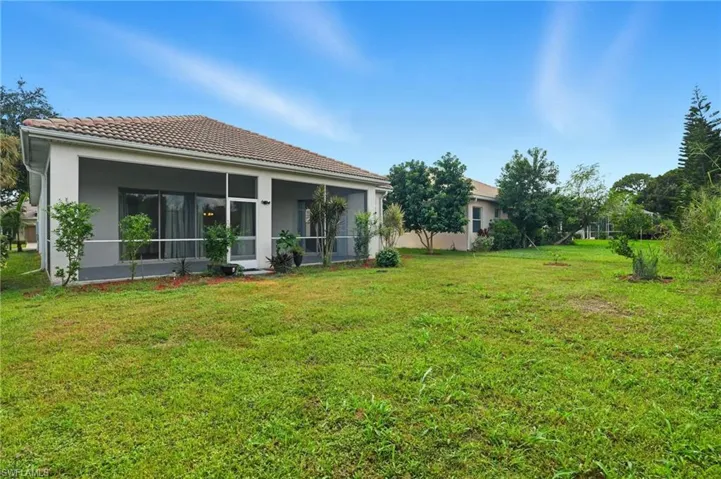 Back of house featuring a sunroom, a yard, stucco siding, and a tile roof - Virtually Edited Image