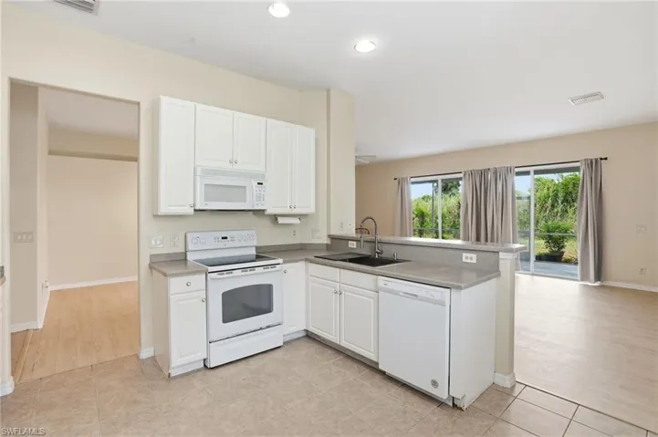 Kitchen featuring white appliances, white cabinetry, light tile patterned floors, a peninsula, and recessed lighting - Virtually Edited Image