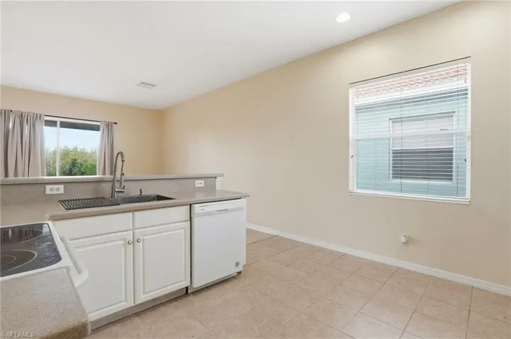 Kitchen featuring white cabinets, white appliances, light tile patterned flooring, recessed lighting, and light stone counters - Virtually Edited Image