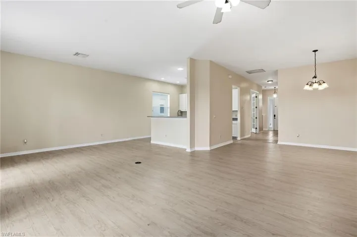 Unfurnished living room with light wood finished floors, a chandelier, ceiling fan, and recessed lighting - Virtually Edited Image