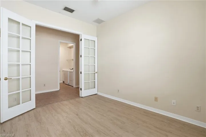 Empty room featuring light wood-style flooring, french doors, and washer and dryer - Virtually Edited Image