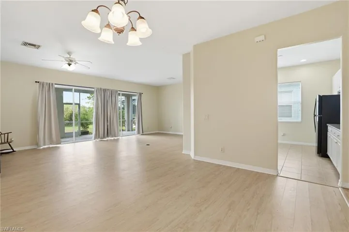 Unfurnished room featuring a chandelier, light wood finished floors, healthy amount of natural light, and a ceiling fan - Virtually Edited Image