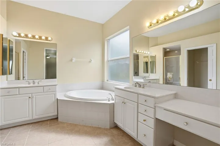 Full bathroom featuring two vanities, light tile patterned flooring, a stall shower, a garden tub, and a ceiling fan - Virtually Edited Image