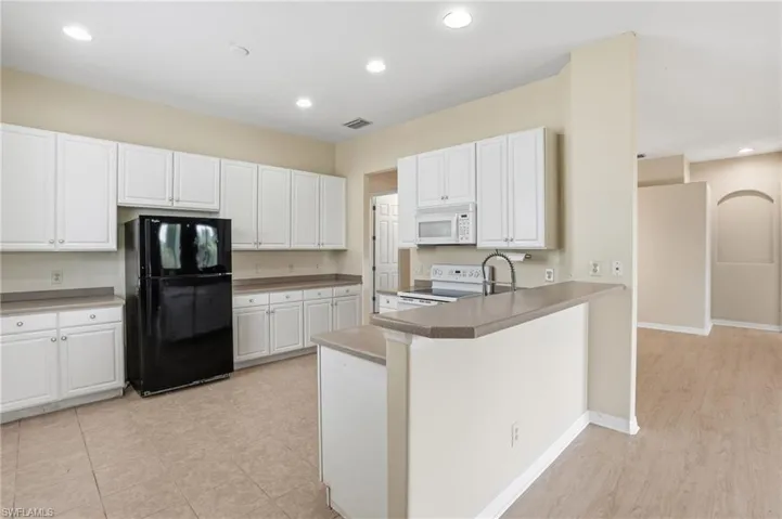 Kitchen with white appliances, white cabinets, recessed lighting, a peninsula, and a breakfast bar - Virtually Edited Image
