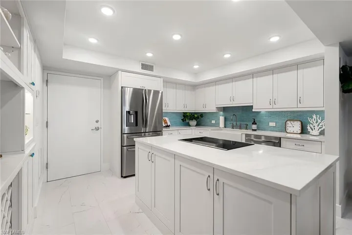 Kitchen with appliances with stainless steel finishes, light tile floors, white cabinets, a center island, and light stone countertops