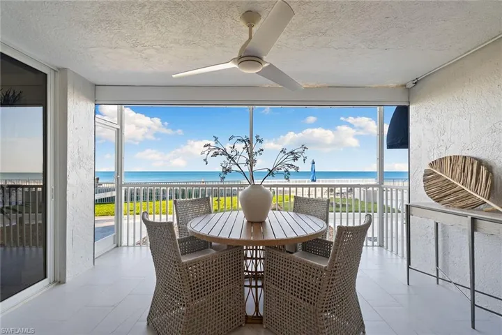 Sunroom with view of water and beach, a textured wall, floor to ceiling windows, and a textured ceiling