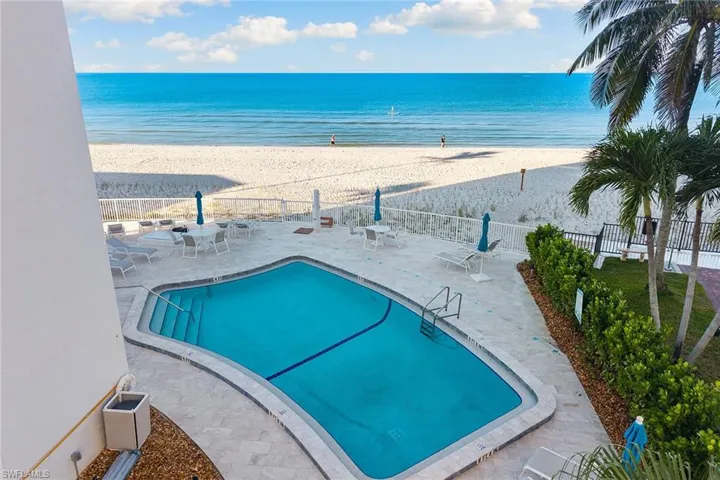 Community pool with a patio and view of water and beach