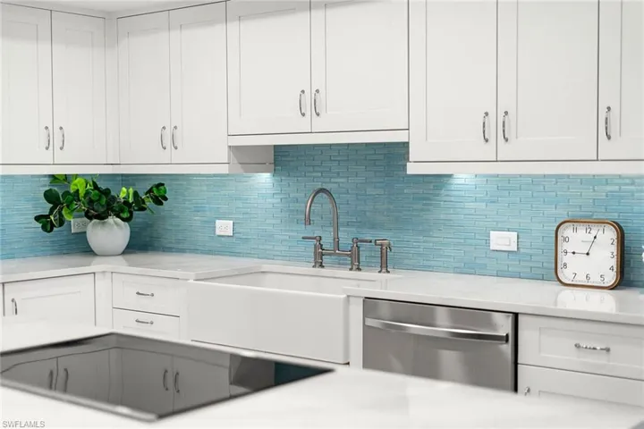 Kitchen with white cabinets, stainless steel dishwasher, black electric stovetop, light stone countertops, and decorative backsplash