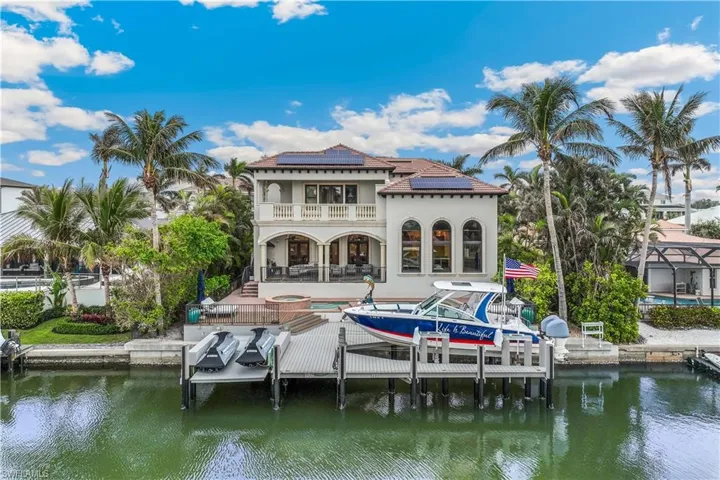 Back of house with a patio area, a balcony, a water view, and solar panels