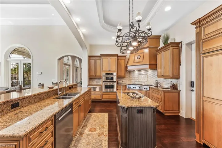 Gourmet kitchen -  featuring light stone countertops, a large island, sink, stainless steel appliances, and dark hardwood / wood-style floors