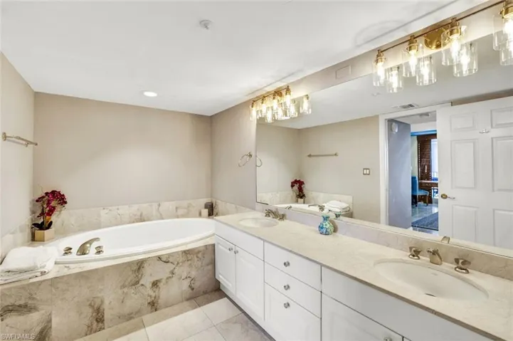 Full bathroom with double vanity, a bath, visible vents, and a sink
