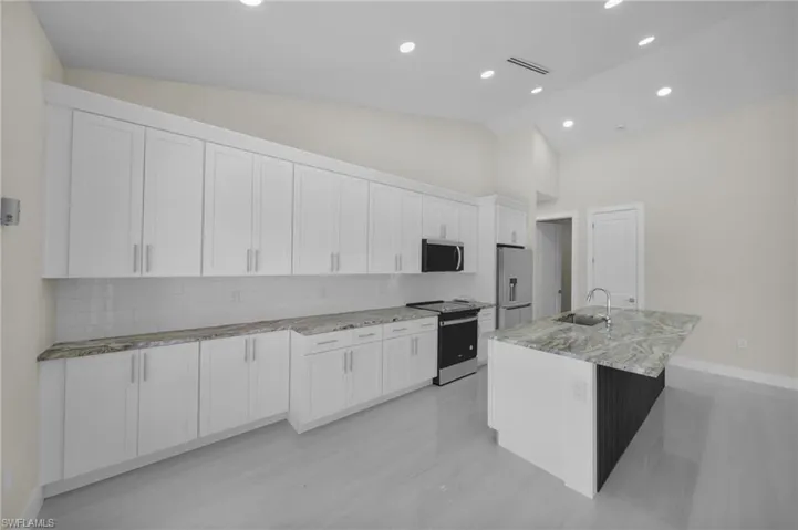 Kitchen with appliances with stainless steel finishes, white cabinets, light stone countertops, backsplash, and recessed lighting