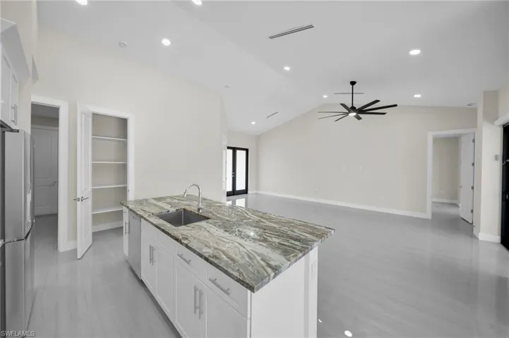 Kitchen with stainless steel appliances, white cabinets, an island with sink, ceiling fan, and light stone countertops