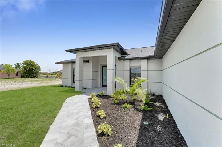 Doorway to property with stucco siding, a lawn, and roof with shingles