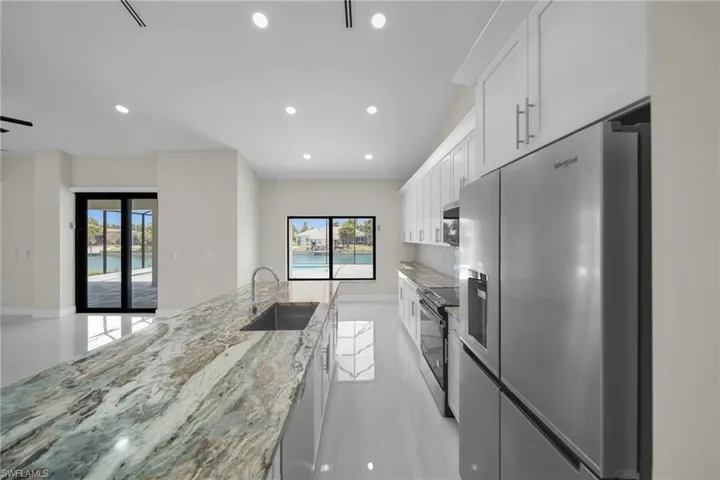 Kitchen featuring appliances with stainless steel finishes, plenty of natural light, recessed lighting, white cabinetry, and light stone counters