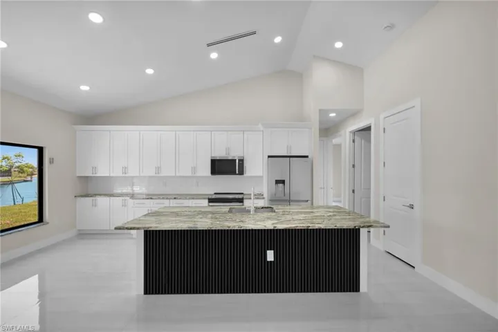 Kitchen with stainless steel appliances, white cabinets, light stone counters, a center island with sink, and high vaulted ceiling