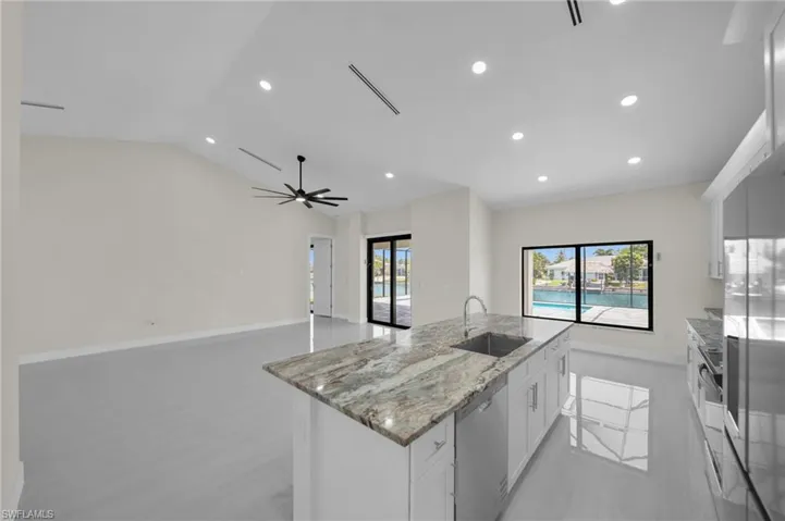 Kitchen featuring stainless steel dishwasher, recessed lighting, lofted ceiling, a center island with sink, and white cabinetry