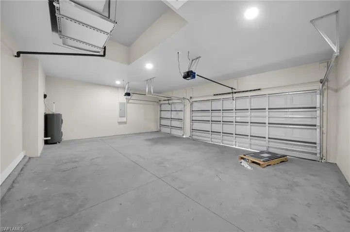 Garage with a garage door opener, electric panel, and recessed lighting