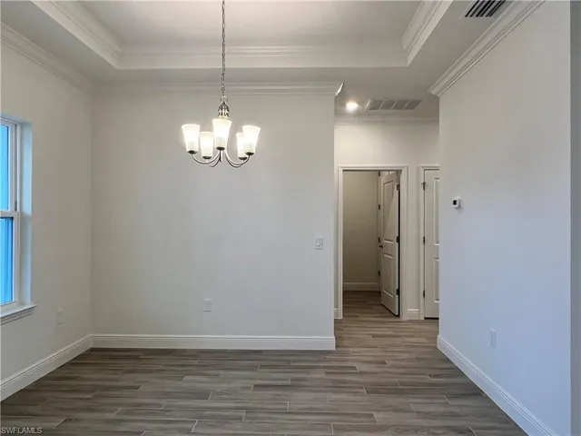 Unfurnished dining area with wood finish floors, a chandelier, and crown molding