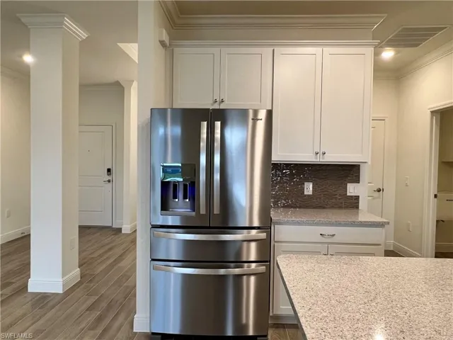Kitchen with crown molding, stainless steel fridge, light stone counters, white cabinetry, and dark wood-style floors