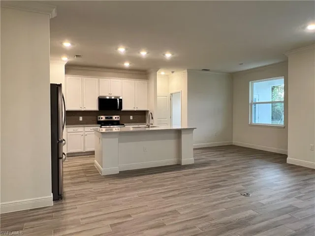 Kitchen featuring white cabinetry, stainless steel appliances, a center island with sink, recessed lighting, and light wood-type flooring