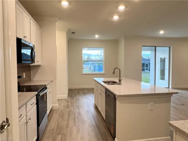 Kitchen with stainless steel appliances, light wood-type flooring, white cabinets, light stone counters, and recessed lighting