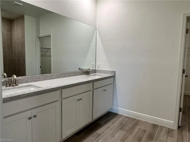 Full bath featuring a walk in closet, a textured wall, double vanity, and wood finish floors
