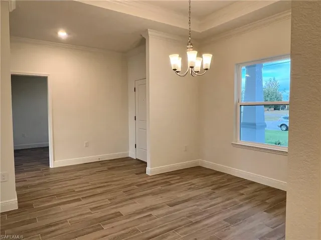 Empty room with wood finished floors, suspended lighting, and ornamental molding